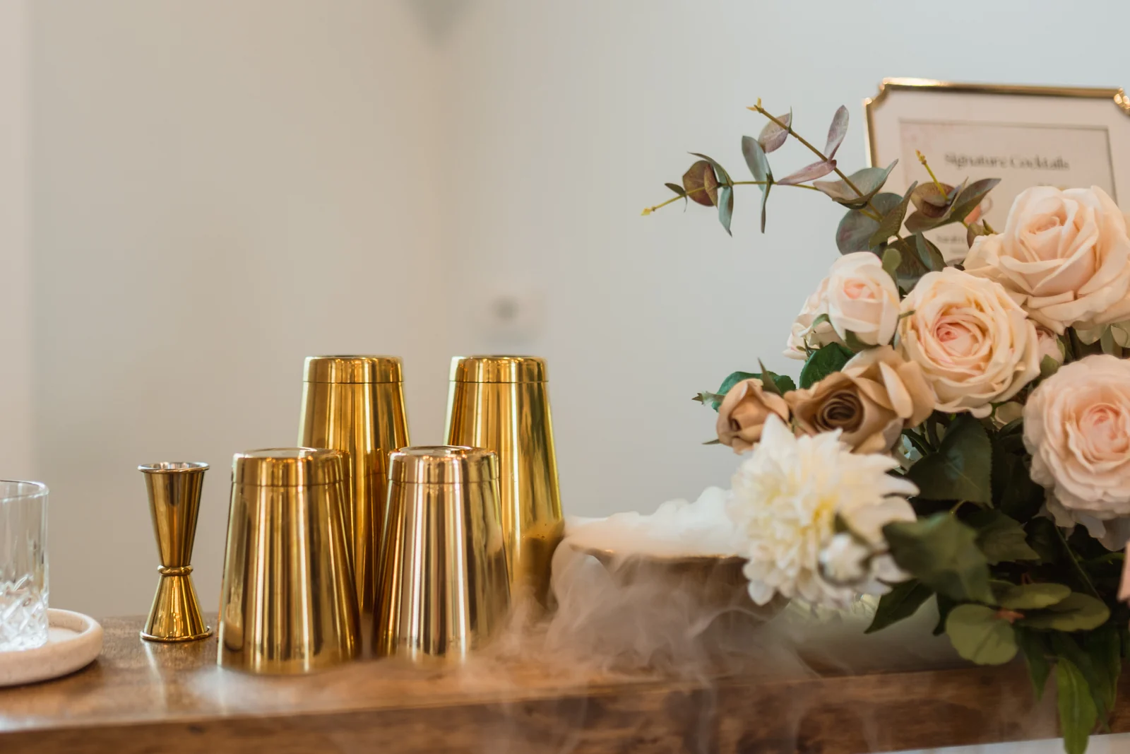 WinterBrooke Bar setup detail — gold cocktail shakers, dry ice, and florals